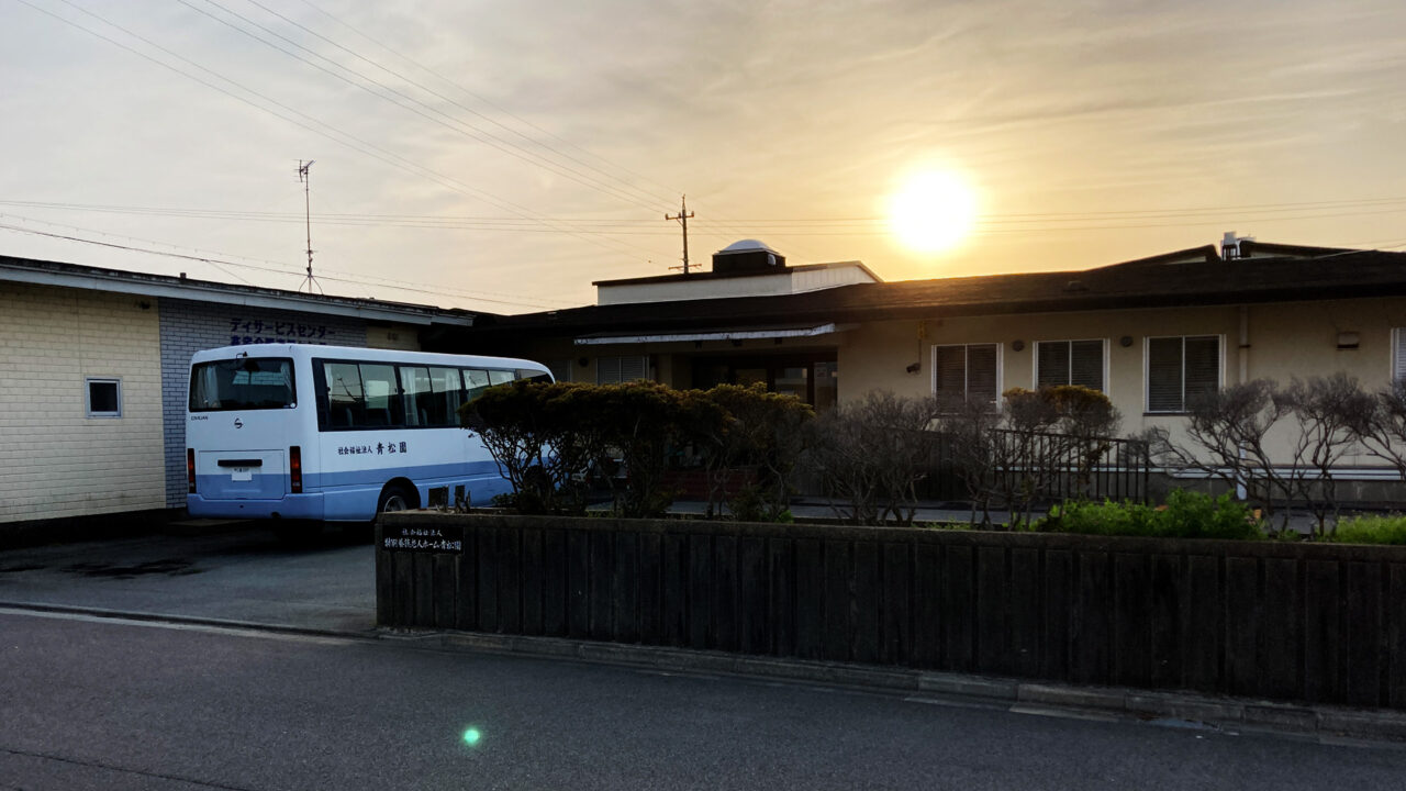 介護施設の建物外観と送迎用マイクロバス、夕焼け時の撮影